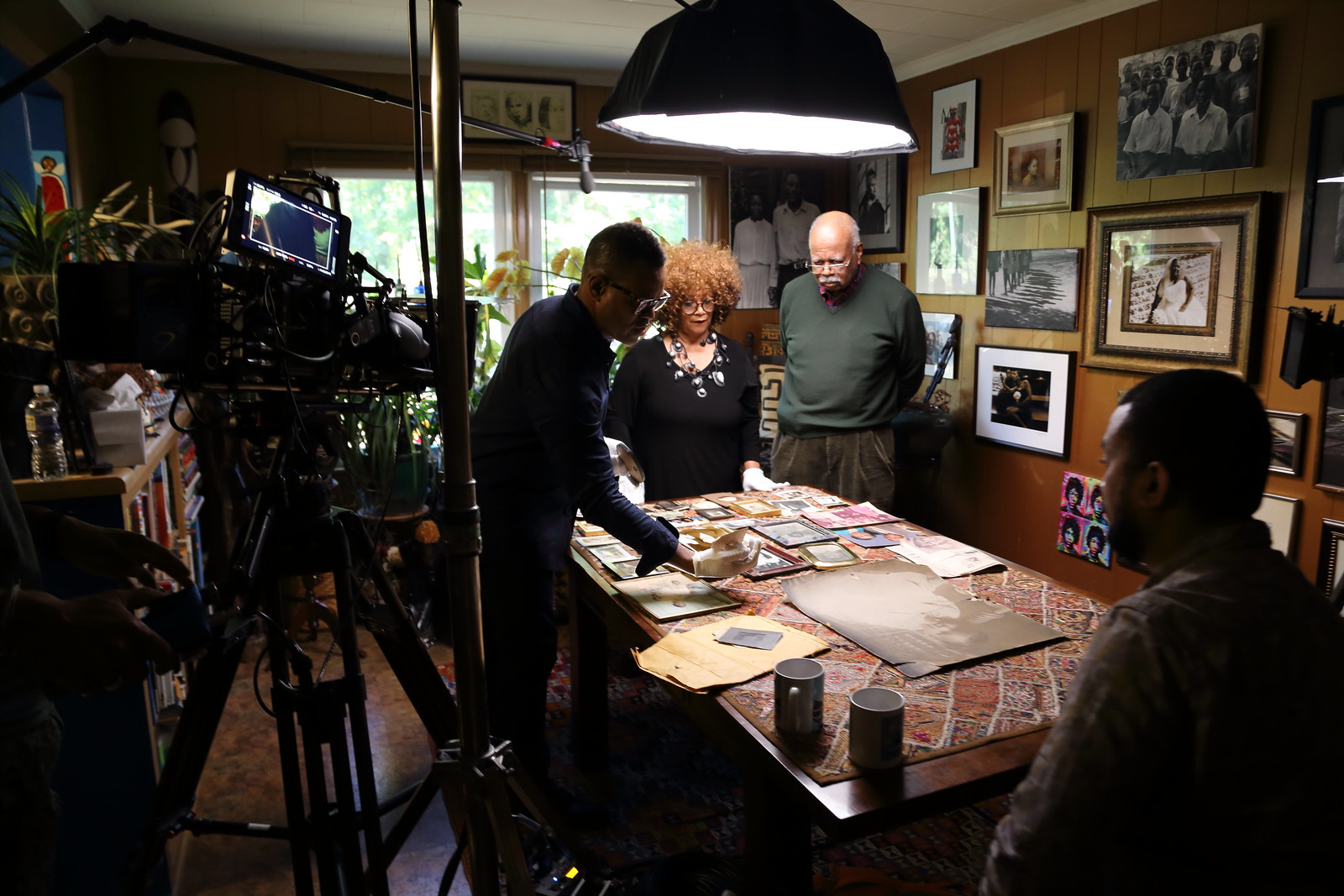 A camera crew recording Thomas Allen Harris interviewing a family in front of a table of family photographs