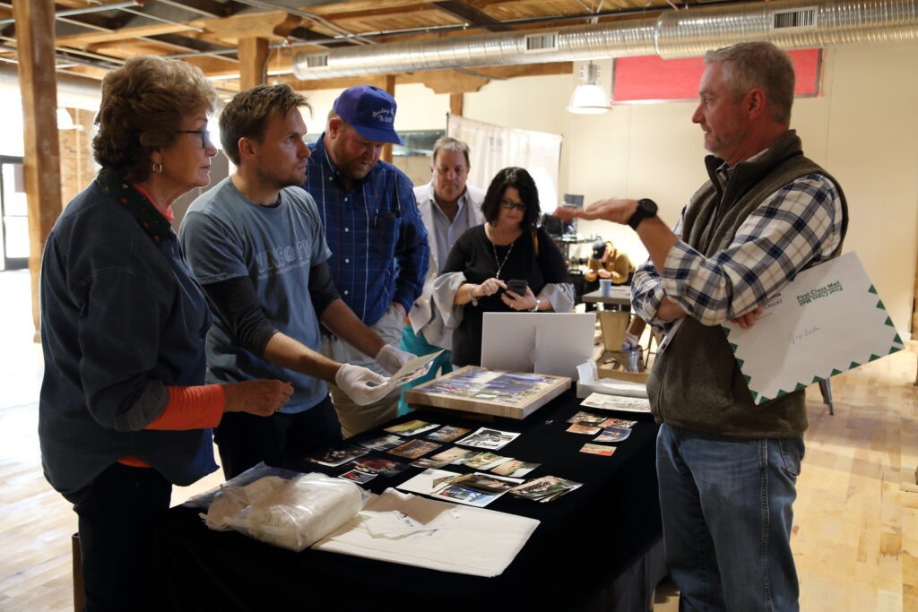 Group of people standing around a table of family photographs examining and discussing them