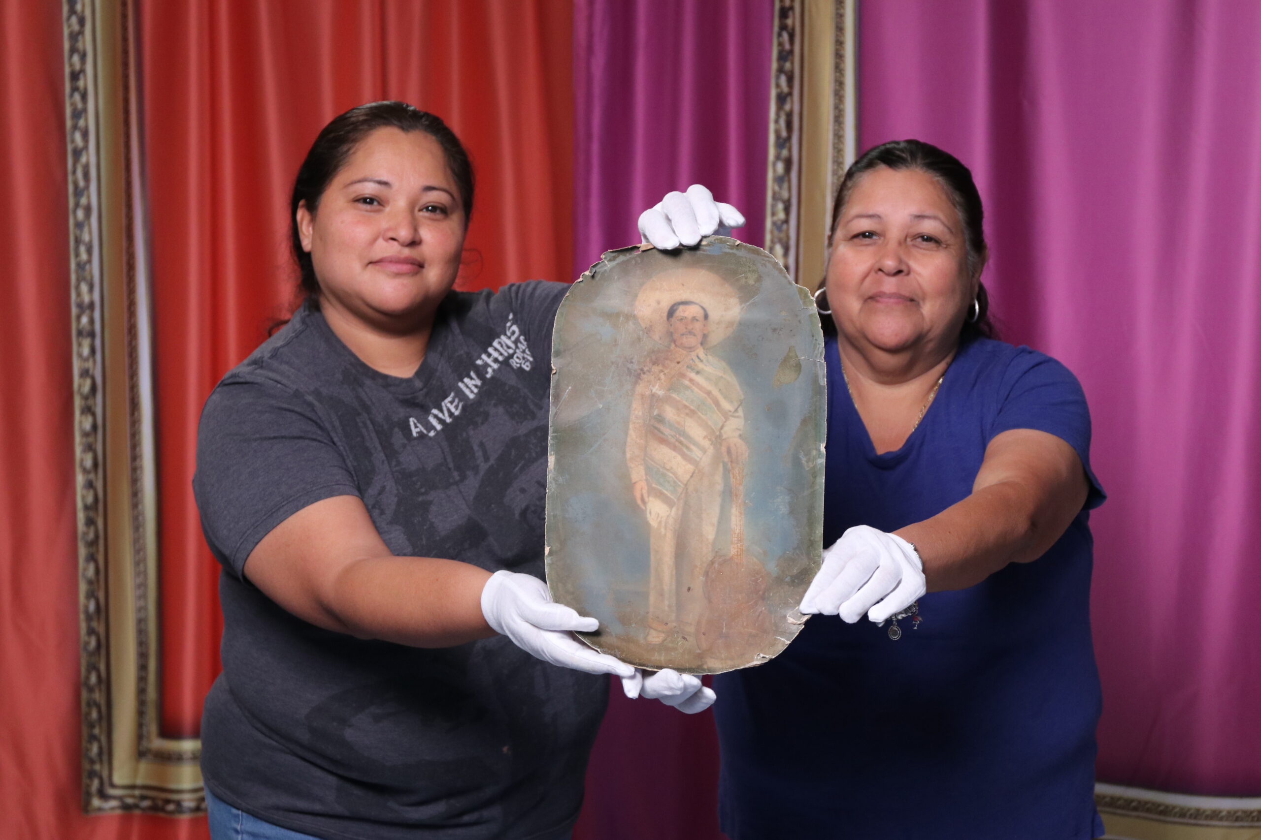 A mother and daughter holding up an archival print of a man in a sombrero holding a guitar