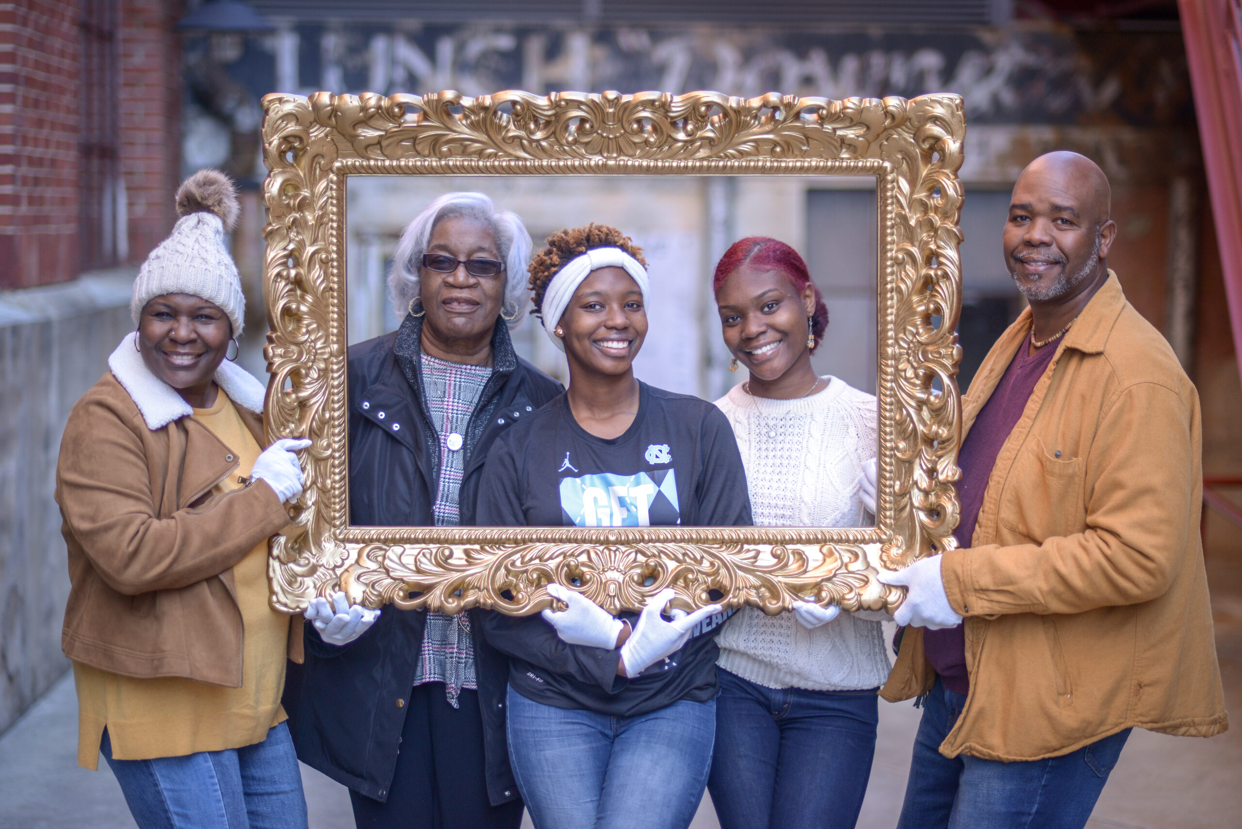 A family smiling and posing, holding an empty ornate frame in front of them