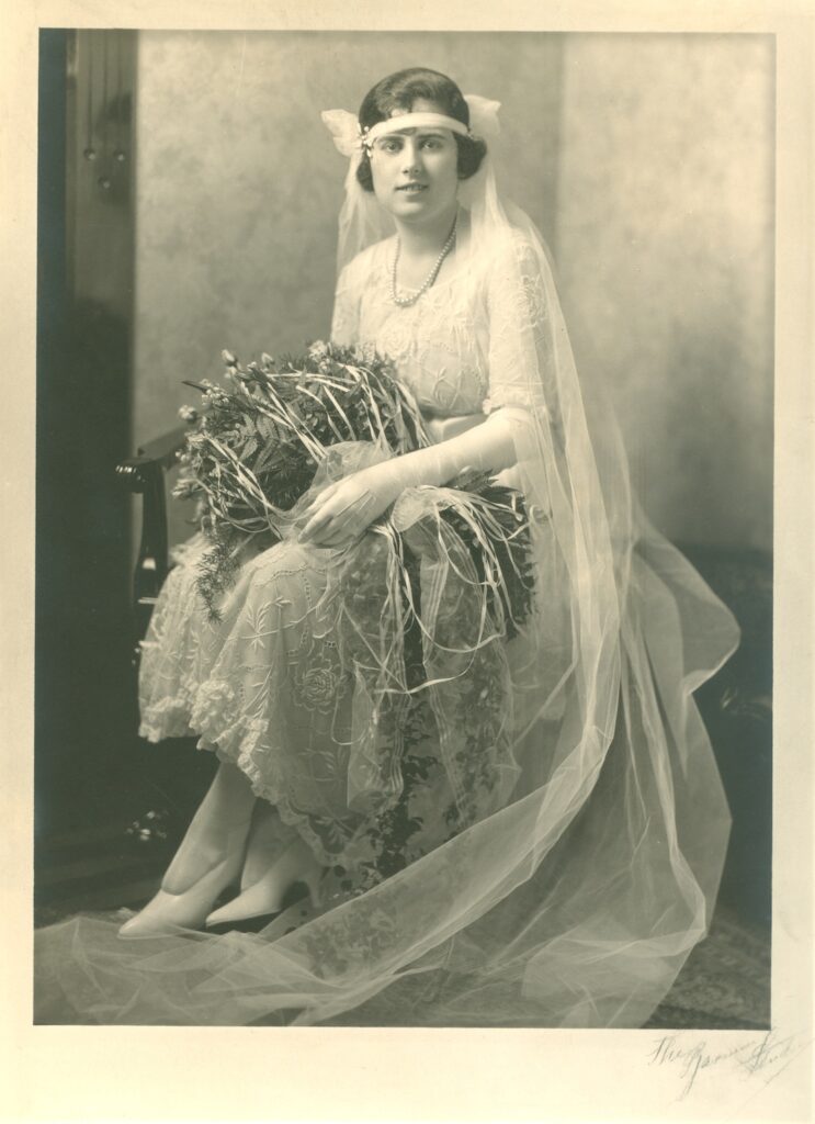 An archival, black and white photograph of a woman in her wedding dress